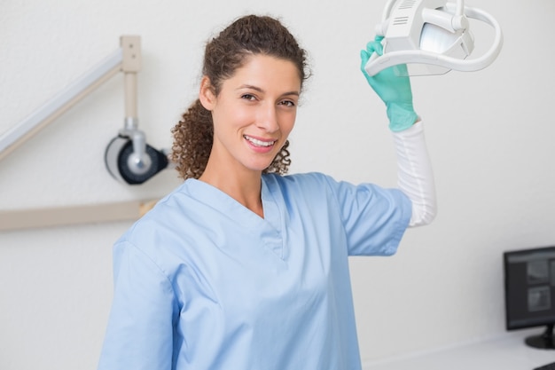 Dentist in blue scrubs smiling at camera beside light