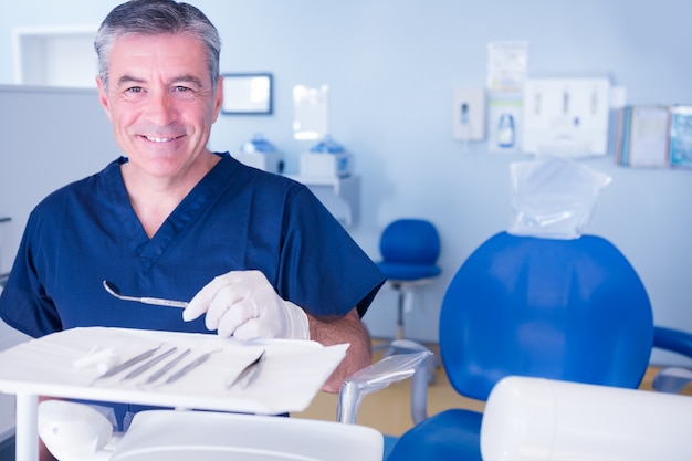 Dentist in blue scrubs smiling at camera holding tools