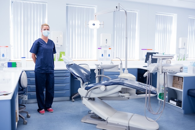 Dentist in blue scrubs standing beside chair