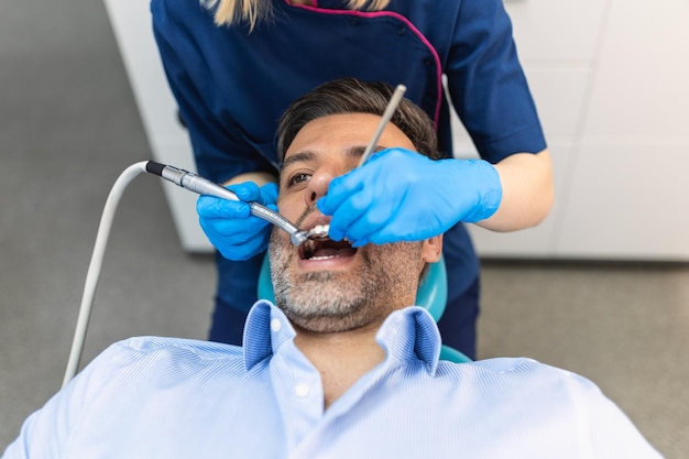 Dentista in uniforme blu che esegue la procedura dei denti al paziente paziente maschio durante la procedura di trattamento nella clinica dentale contemporanea
