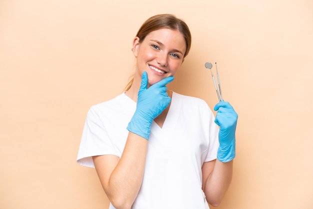 Dentist caucasian woman holding tools isolated on beige background happy and smiling