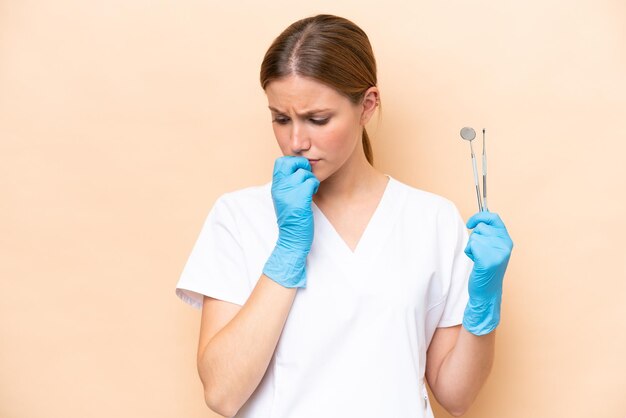 Dentist caucasian woman holding tools isolated on beige background having doubts