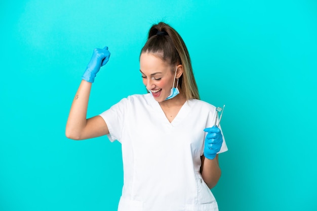 Dentist caucasian woman holding tools isolated on blue background celebrating a victory