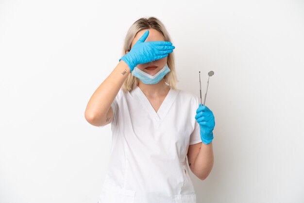 흰색 배경에 격리된 도구를 들고 손으로 눈을 가리고 있는 백인 치과의사 여자