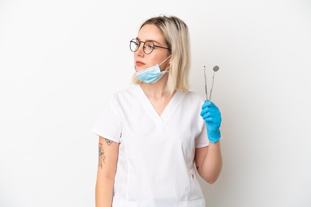 Dentist caucasian woman holding tools isolated on white background looking to the side