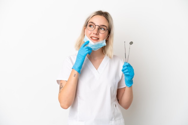 웃는 동안 찾고 흰색 배경에 고립 된 도구를 들고 치과 의사 백인 여자