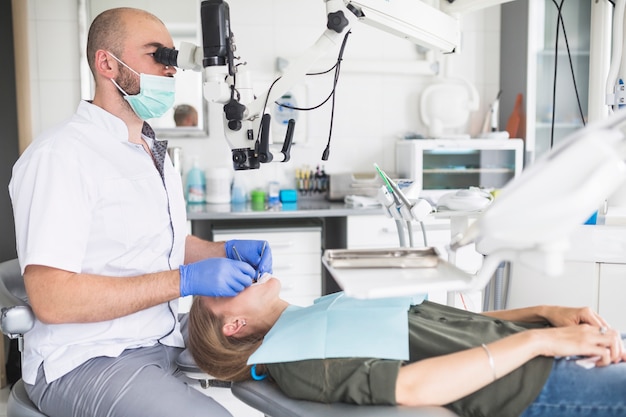 Стоматолог проверяет зубы пациента пациента с помощью стоматологического микроскопа