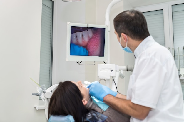 Dentist checking patient's teeth with camera, looking on screen