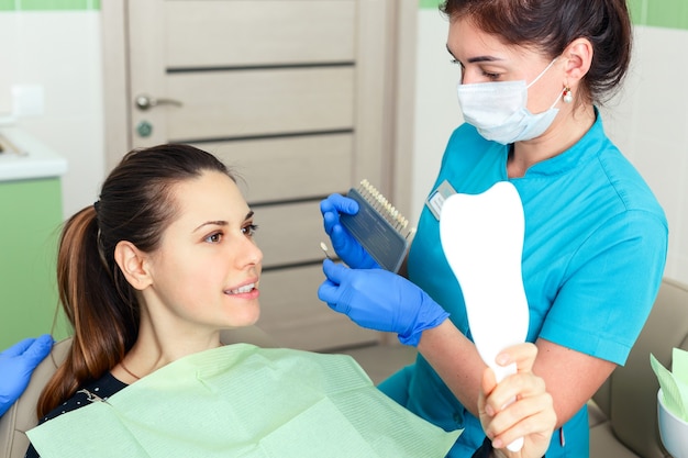 Стоматолог проверяет и выбирает цвет зубов молодой женщины