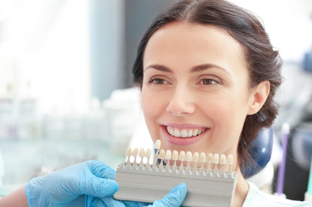 Dentist checking and selecting color of young woman's teeth