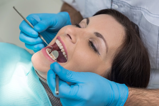 Dentista che controlla i denti della donna con lo specchio durante la visita