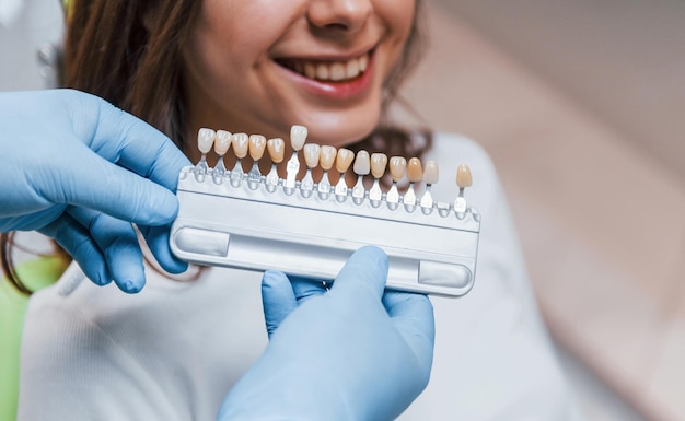 Dentist checks level of teeth whitening with color. Young adult woman have a visit in the clinic.