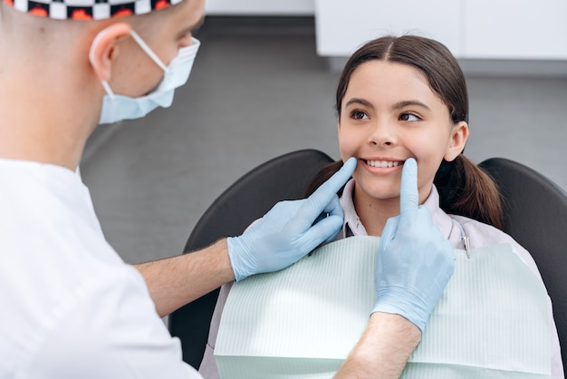 치과 의사는 젊은 환자의 치아를 확인합니다. 치과 방문에 매력적인 어린 소녀