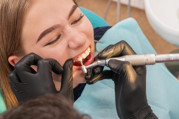 dentist cleans teeth of a patient sitting in the chair by means of a drill with a brush