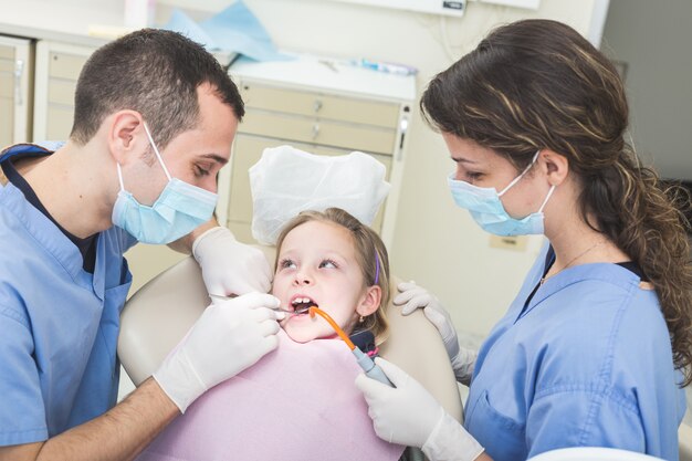 Dentist and dental assistant examining young girl teeth