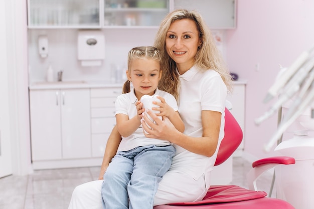 Dentist doctor holding a little girl in her arms in the dental office