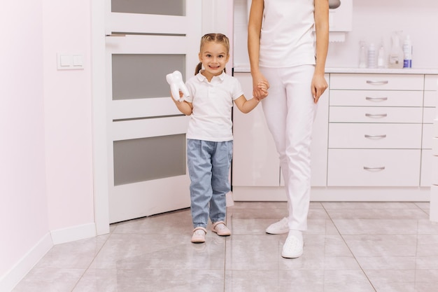 The dentist doctor holds the little girl by the hand and leads her to the dental office