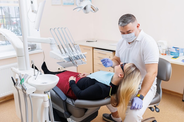 The dentist doctor looks at the patient's teeth and holds dental instruments near the mouth The assistant helps the doctor They wear white uniforms with masks and gloves Dentist Dental office