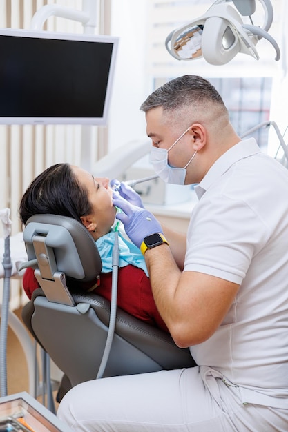 The dentist doctor looks at the patient's teeth and holds dental instruments near the mouth The assistant helps the doctor They wear white uniforms with masks and gloves Dentist Dental office