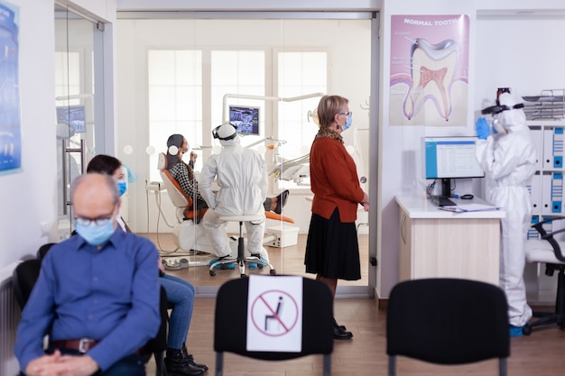 Dentist doctor in ppe suit consulting patient in dental clinic dressed in ppe suit as safety precation during global pandemic with coronaivurs