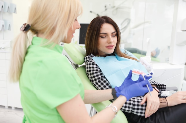 Dentist doctor shows the patient a jaw model and talks about the upcoming treatment.