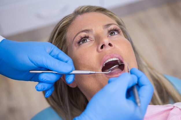 Dentista che esamina un paziente femminile con gli strumenti