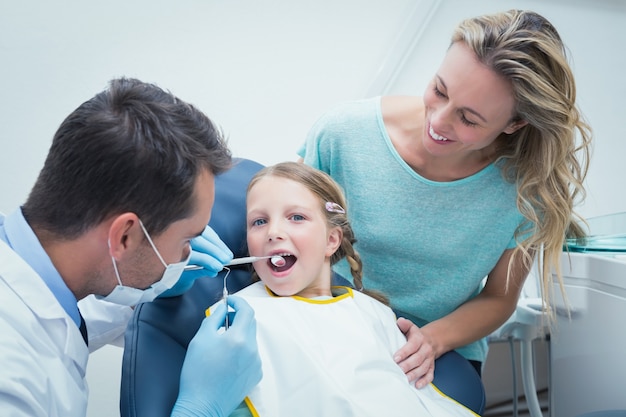 Dentista che esamina i denti delle ragazze con l'assistente