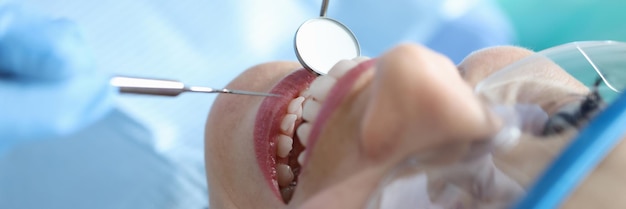 Dentist examining oral cavity of woman patient in clinic using tools closeup