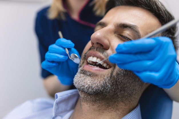 Dentista che esamina i denti di un paziente nello studio del dentista uomo paziente che ha un trattamento dentale presso lo studio del dentista