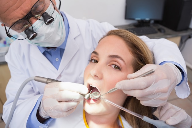 Dentist examining a patients teeth in the dentists chair with assistant