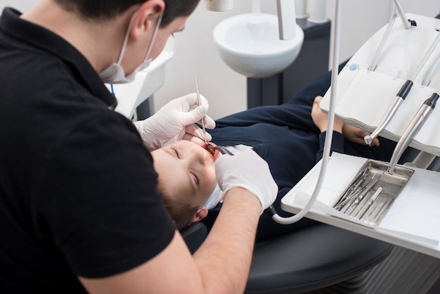 歯科医が歯科用ツールを使用して歯科医院で少年患者の歯を調べる