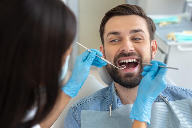 Dentist examining teeth of handsome smiling client in dental chair