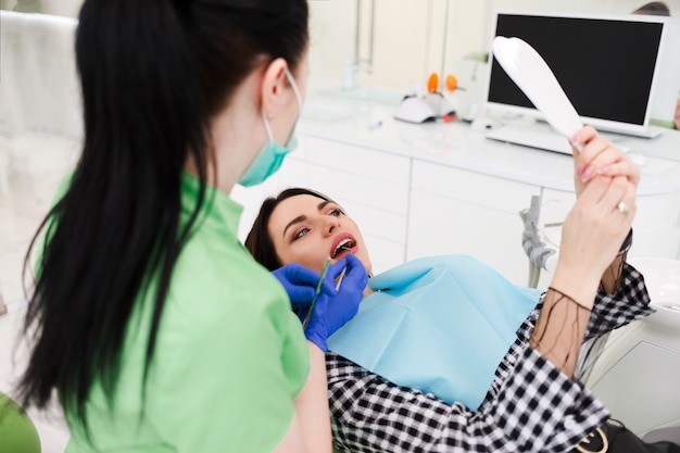 Dentist examining teeth for patient. Girl looks in the mirror at the process of checking teeth