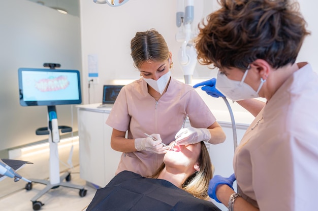 Dentist examining the teeth of a woman reclining on chair in a dental clinic