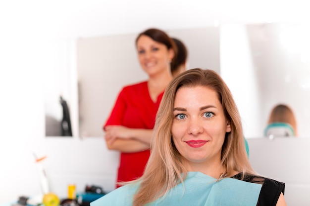 Dentist finishing successful teeth restoration black haired doctor in green mask giving to happy patient mirror beautiful longhaired woman looking at pristine white teeth with great pleasure