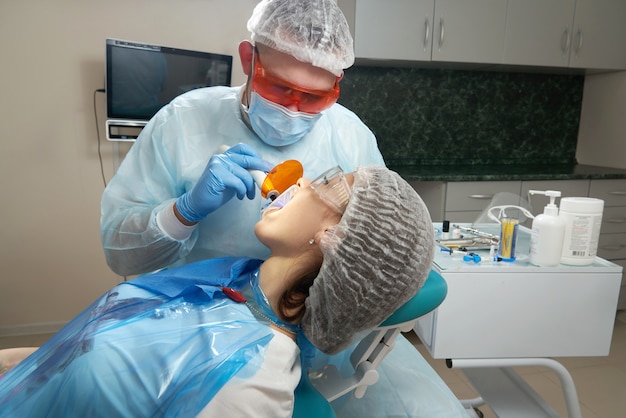 Dentist in glove with dental curing light working with female client