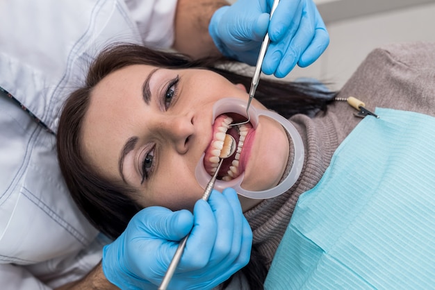 Mani del dentista con strumenti e primo piano del viso del paziente