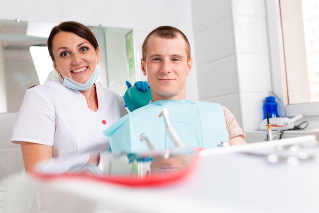 歯科医と彼女の幸せな患者はカメラを見て笑顔します。歯医者でのレセプション、健康な歯、幸せな患者、美しい歯。