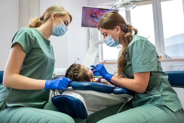 치과 의사와 그의 조수는 카메라로 아이의 치아를 검사하고 화면에 그림을 표시합니다. 치과에서 아이를 검사하는 개념