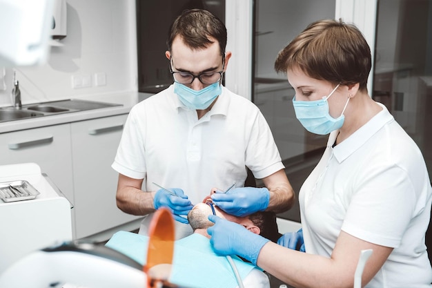 Foto il dentista e il suo assistente curano un paziente maschio in una clinica odontoiatrica