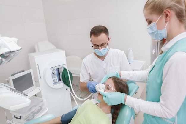 Dentist and his assistant using inhalation sedation on young girl before dental treatment