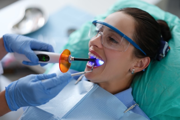 Dentist holds led dental lamp and instrument in patient mouth