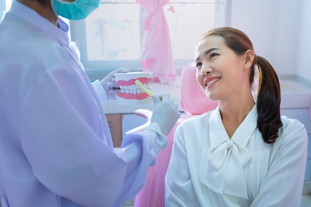 The dentist is demonstrating how to brush teeth for the patients sitting on the dental chair in her clinic.