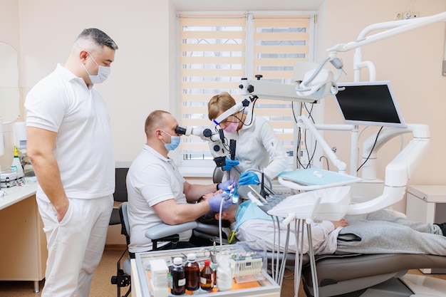 The dentist is in his dental office A dentist in a white uniform treats a patients teeth with a dental microscope Dental office