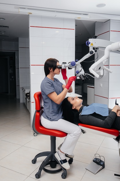 The dentist looks through a microscope and performs surgery on the patient.