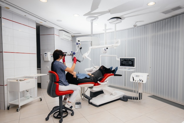 The dentist looks through a microscope and performs surgery on the patient.