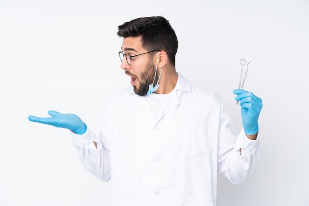 Dentist man holding tools on white wall holding blank space on the palm