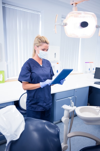 Dentist in mask and blue scrubs using her tablet