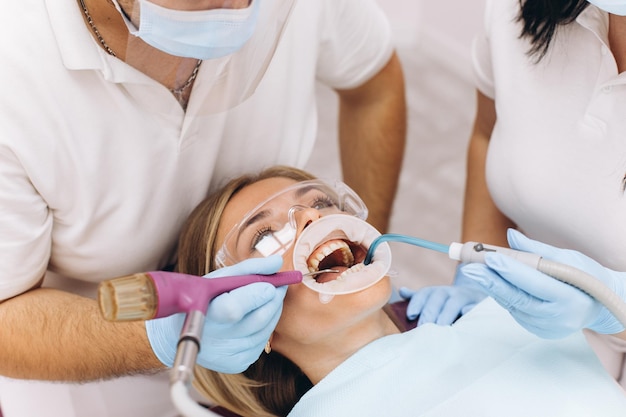 A dentist in a mask and goggles treats a woman's teeth