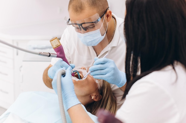 A dentist in a mask and goggles treats a woman's teeth